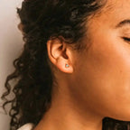 a close up of a person wearing a pair of green onyx and yellow gold triangle shaped stud earrings
