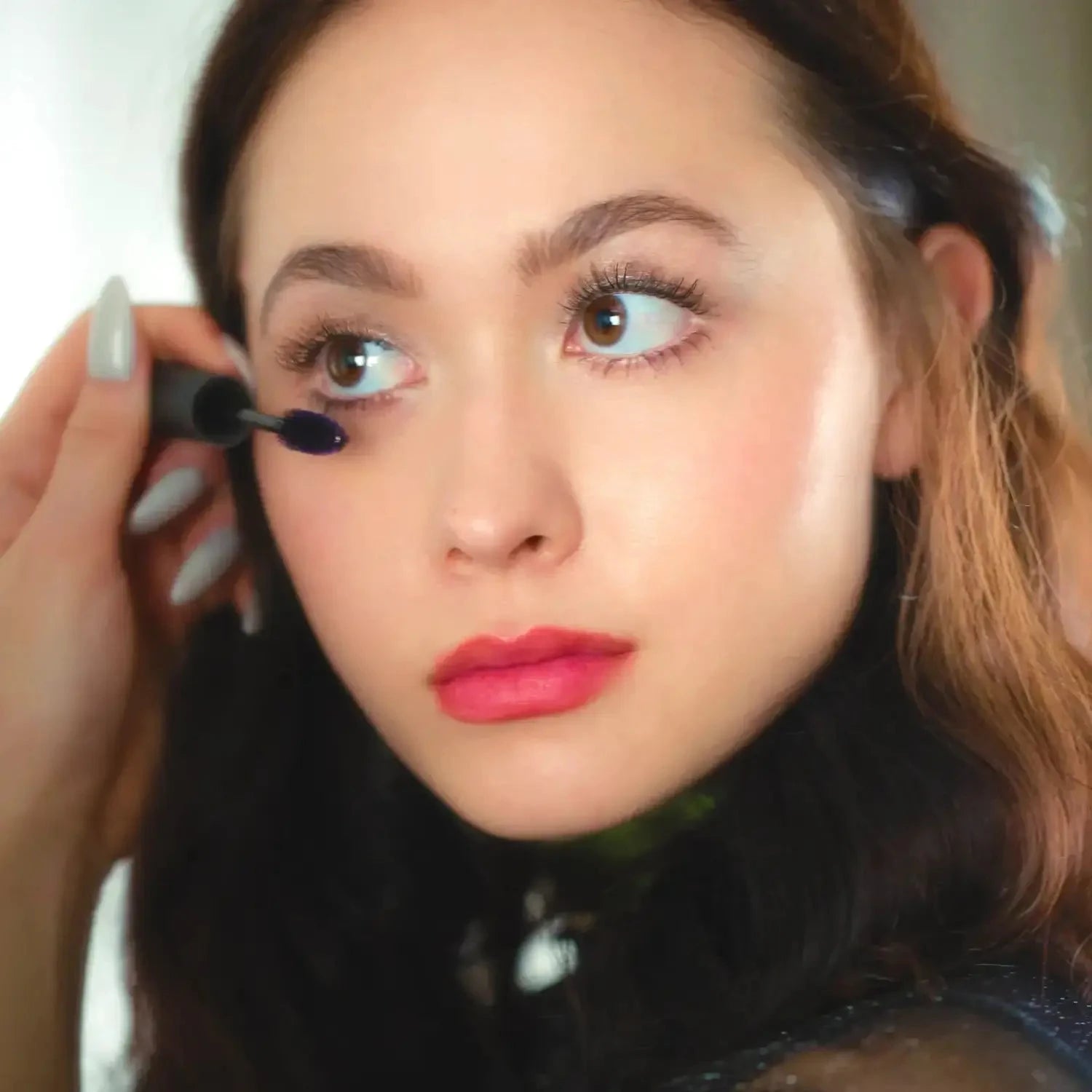 Woman applying Lashfood Conditioning Drama Clean Mascara to lower lashes, showcasing volumizing and lengthening effect for sensitive eyes.