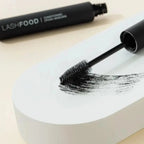 LASHFOOD Mascara in black shown with a swipe of the clean formula and large Bristle Brush on a white surface