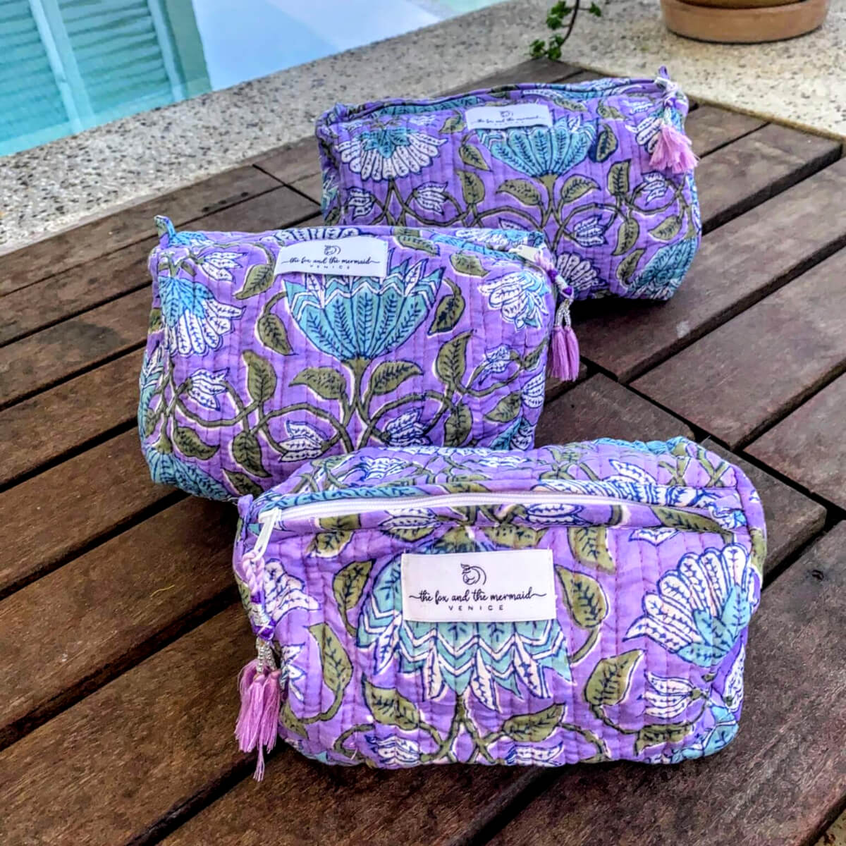 a set of three purple floral toiletry and cosmetics bags of varying sizes with zippers and decorative tassel pulls