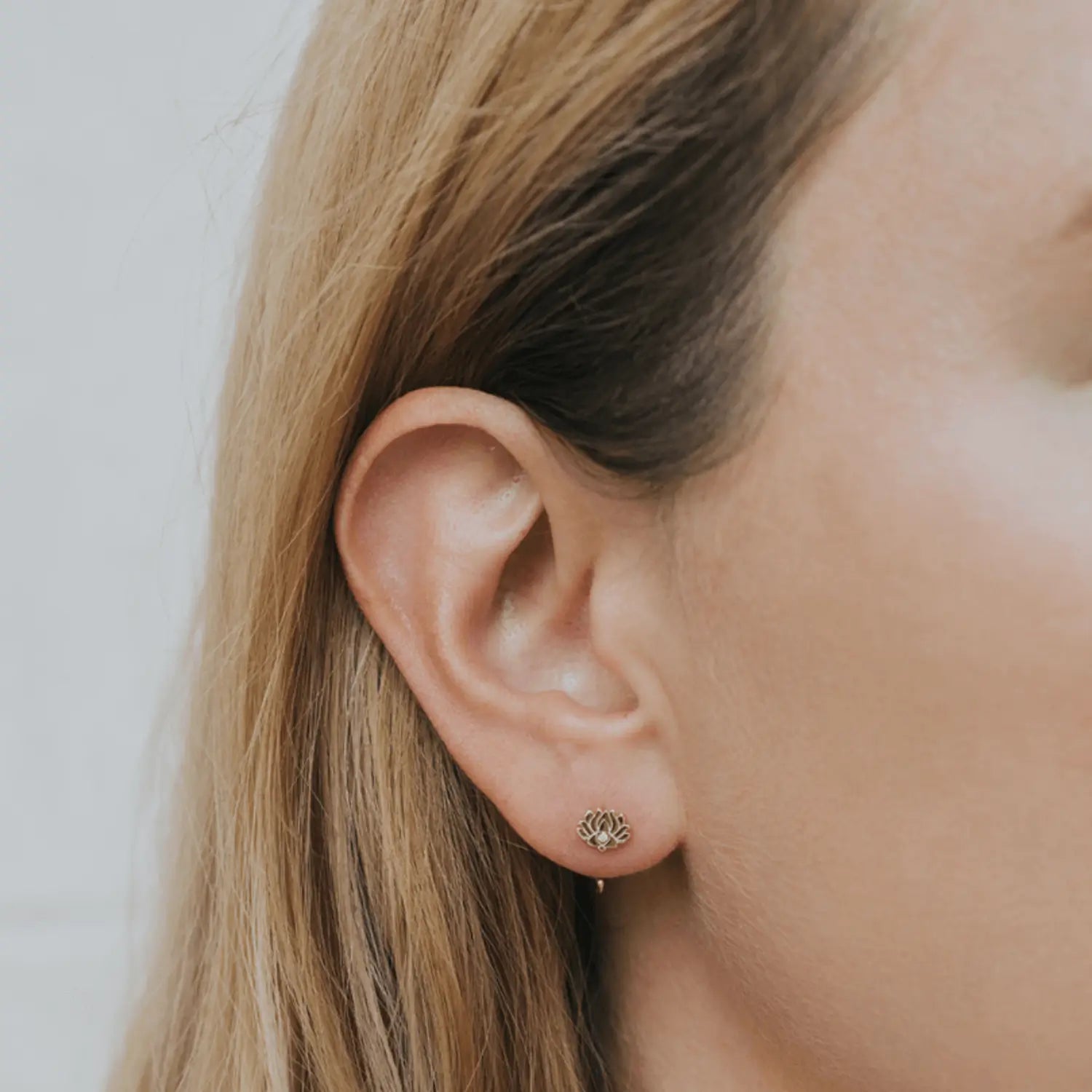 a close up of a person wearing a pair of gold lotus flower earrings