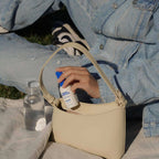 Person with a beige handbag, water bottle, and travel size hypochlorous acid spray bottle.