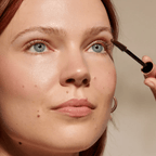 a woman with blue eyes applying minori mother of lashes mascara with the defining and  lengthening bristle brush.