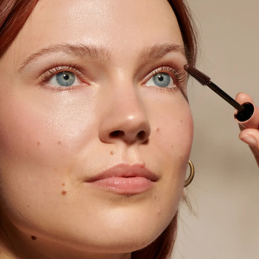 a woman with Fair skin and blue eyes applying minori mother of lashes mascara with the defining bristle brush