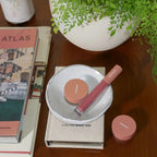 a minori vegan lip gloss in blossom pink in a dish next to minori cosmetics