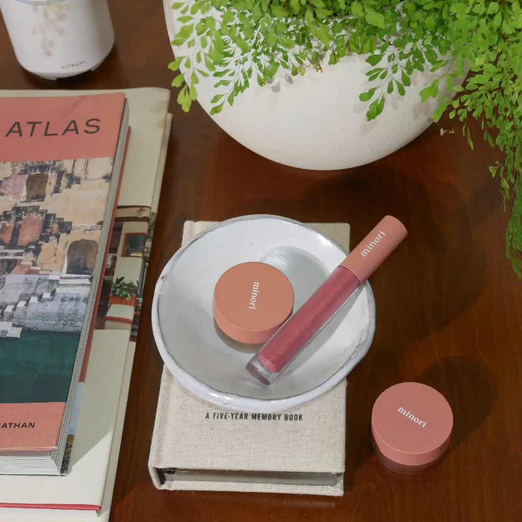 a minori vegan lip gloss in blossom pink in a dish next to minori cosmetics