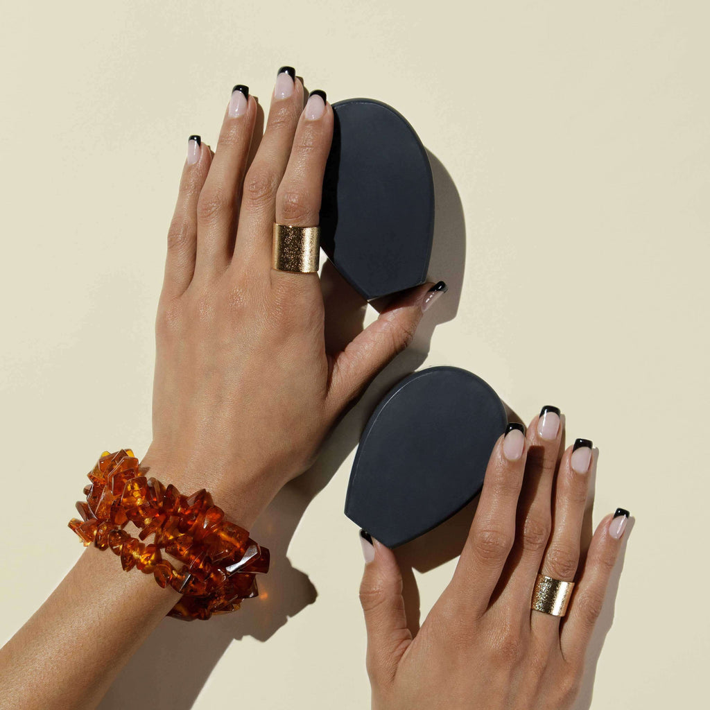 Two hands each holding bars of nopalera noche clara cactus charcoal soap against a beige background
