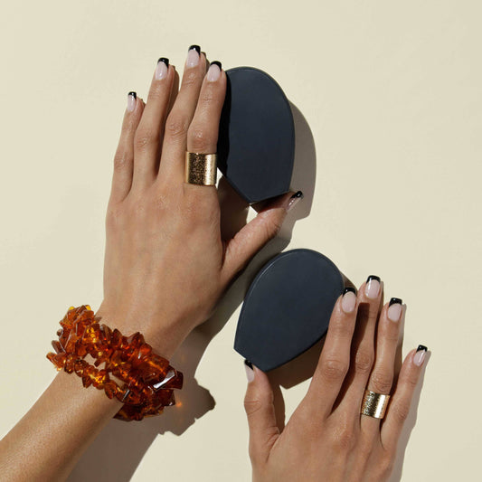 Two hands each holding bars of nopalera noche clara cactus charcoal soap against a beige background