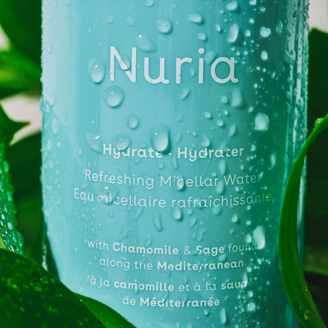 Nuria refreshing micellar water bottle with water droplets on a green leaf background
