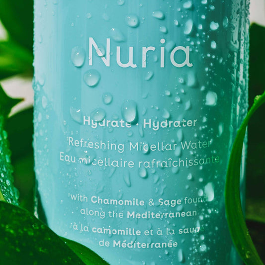 Nuria refreshing micellar water bottle with water droplets on a green leaf background