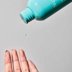 Nuria Beuaty Hydrating Toner for facial skin in a turquoise bottle pouring a drop of liquid onto a hand against a gray background