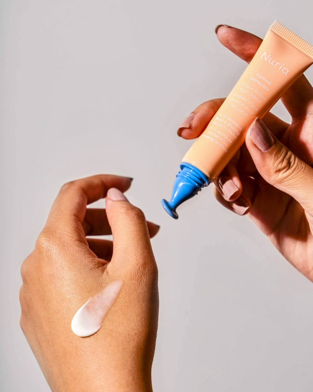 Hand applying Nuria Eye Cream with a drop of cream on the skin, demonstrating its lightweight and nourishing consistency.