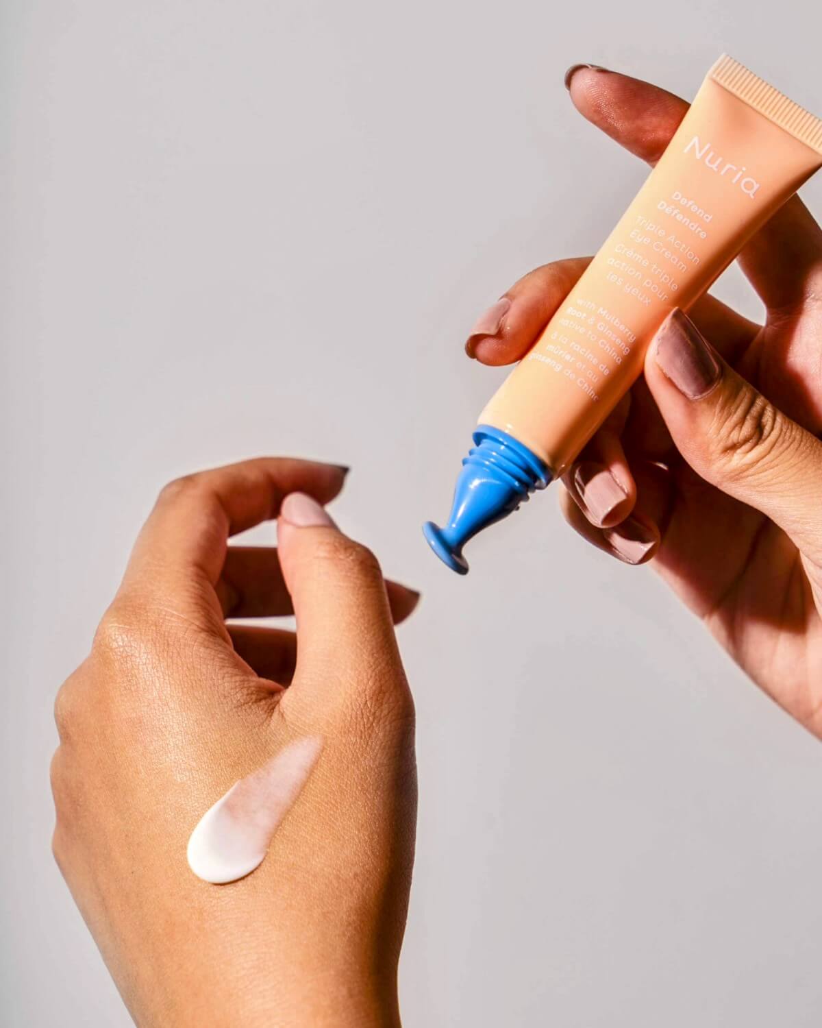 Hand applying Nuria Eye Cream with a drop of cream on the skin, demonstrating its lightweight and nourishing consistency.