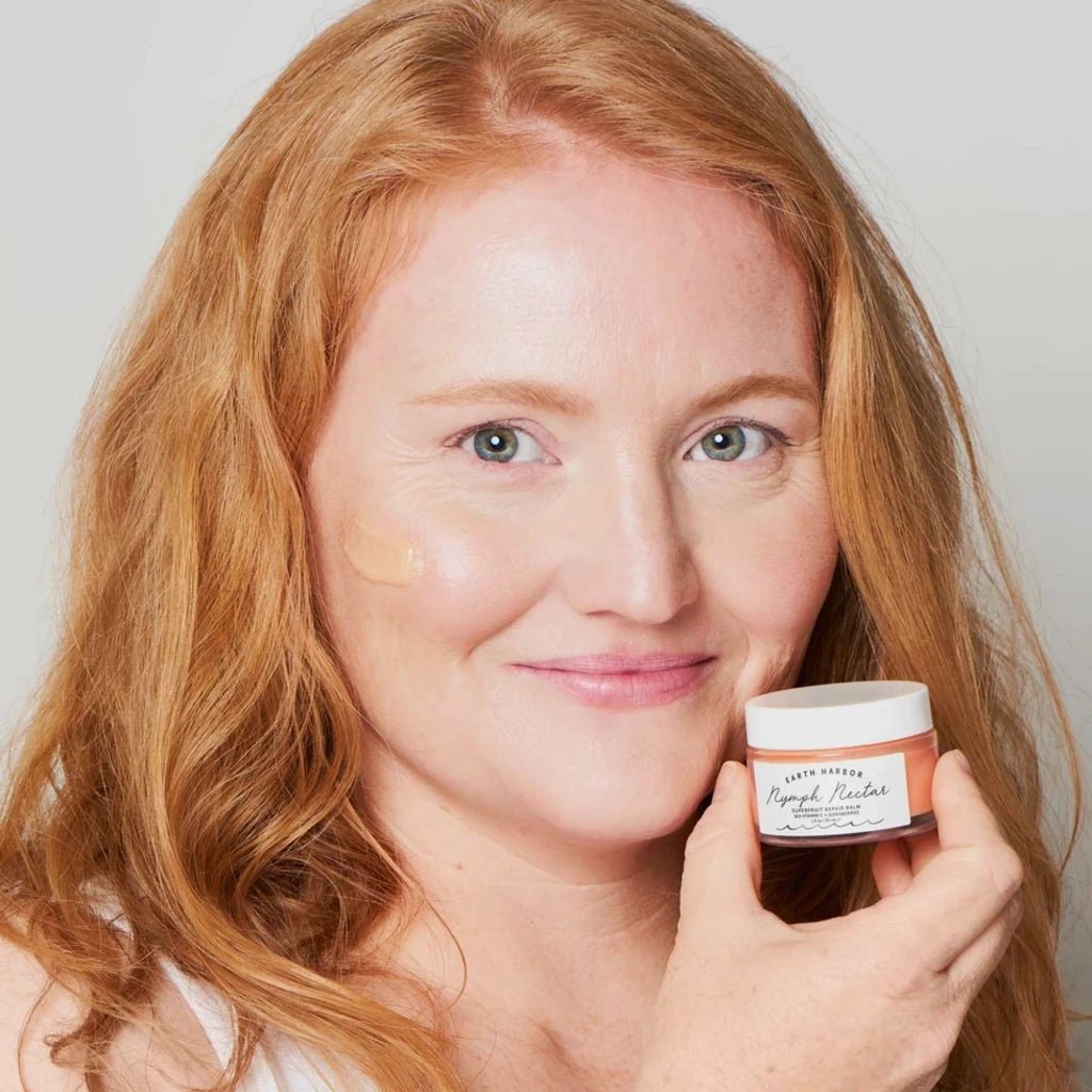 A woman with long red hair holds a small jar of earth harbor nymph nectar balm