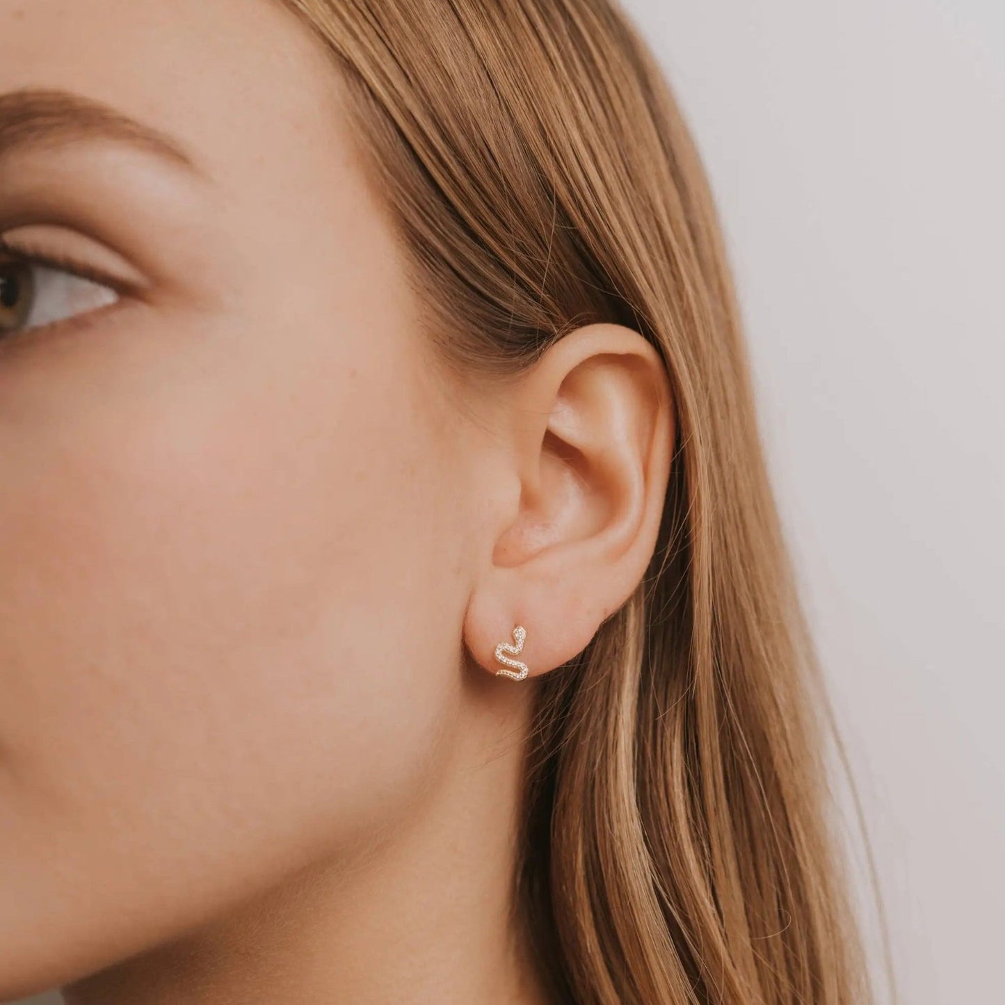 a close up of a person wearing a pair of gold snake earrings