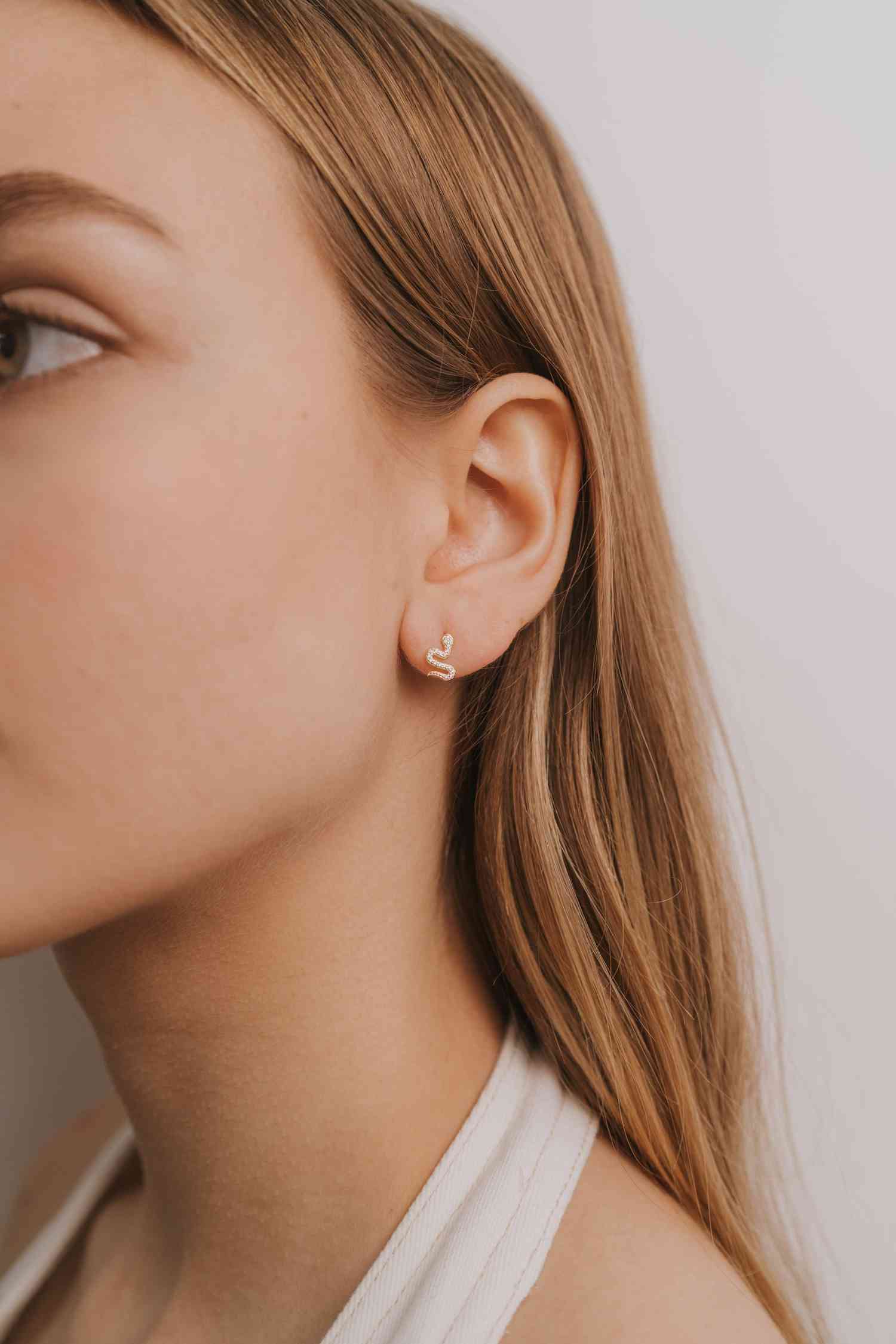 a close up of a person wearing a pair of gold snake earrings