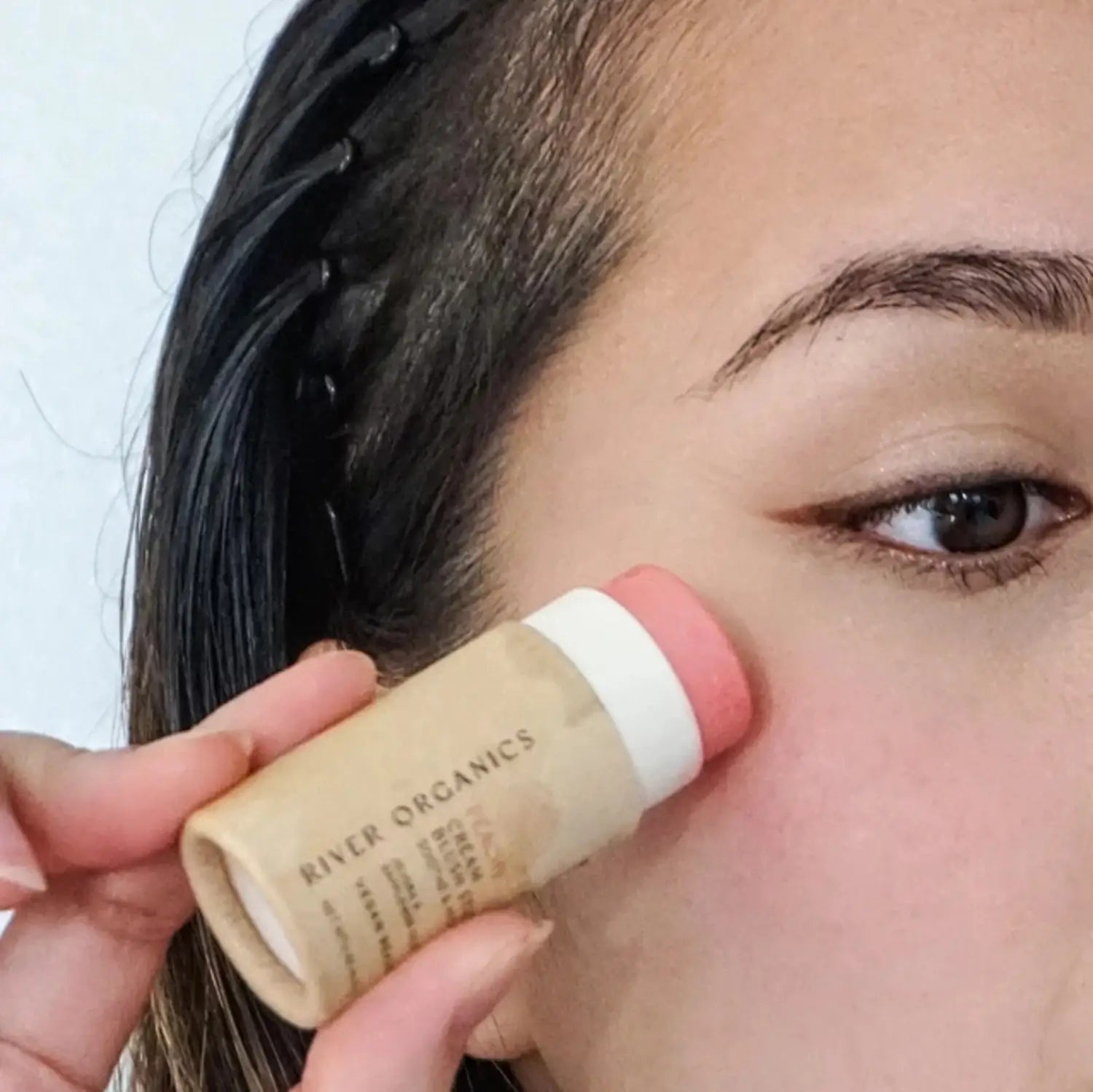 peach blush stick in eco-friendly tube being applied to cheeks