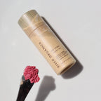Lip balm in an eco-friendly paper tube with pink lip balm on a brush on a white background