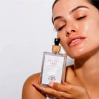 a woman holding a bottle of the Organic Skin Co.'s set the tone rose mist toner to her face showcasing the hydrating formula.