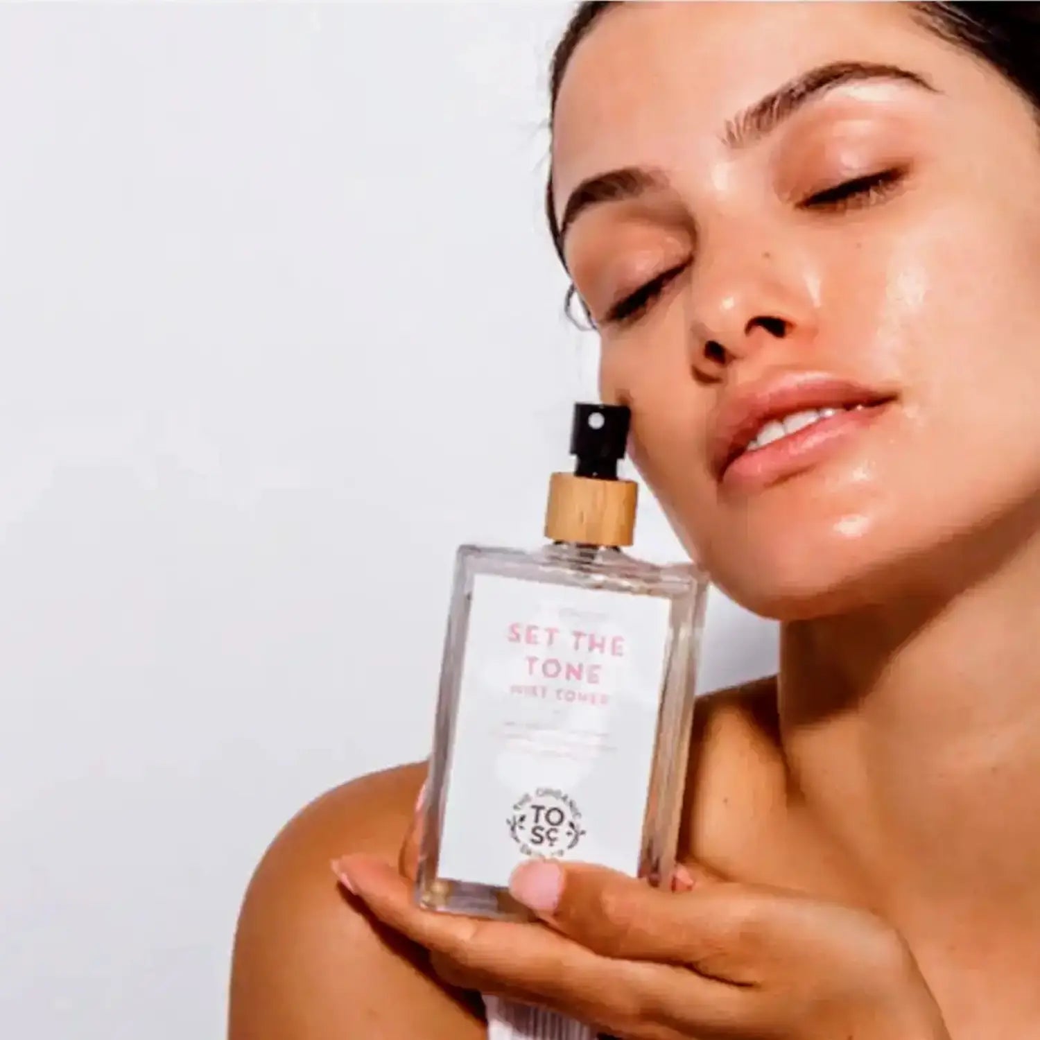 a woman hold a bottle of the Organic skin Co set the tone rose mist toner