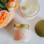 a vanilla rose quartz candle jar with pink gemstones sitting next to a rose bouquet