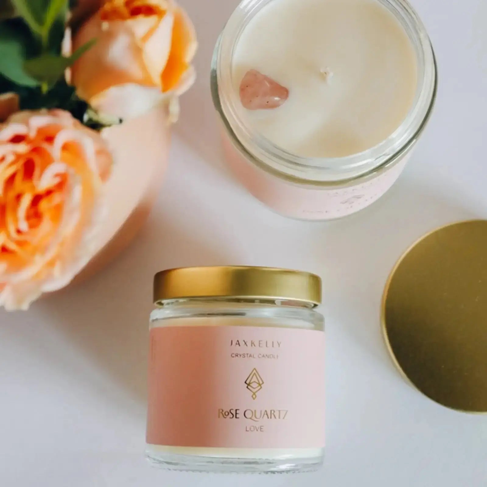 a vanilla rose quartz candle jar with pink gemstones sitting next to a rose bouquet