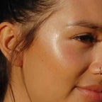 rose quartz pink cream highlighter shown on a cheek of woman with tan skin highlighting the rose quartz shimmer and dewy glow