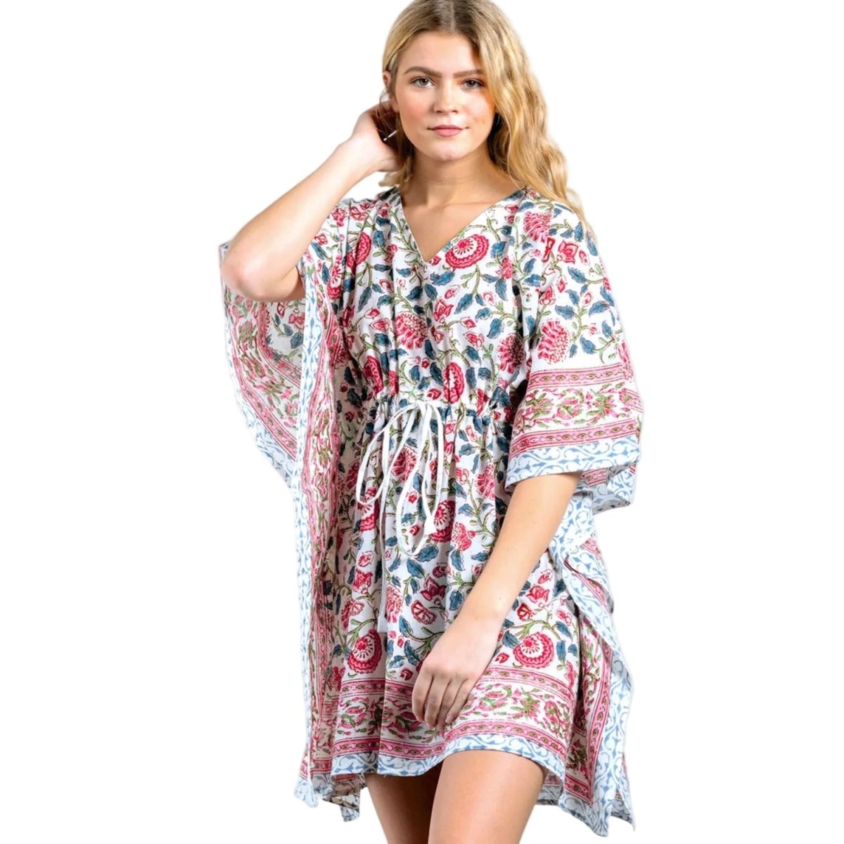 A woman modeling a short kaftan-style dress with a blue, red, and pink floral paisley print against a light gray background.