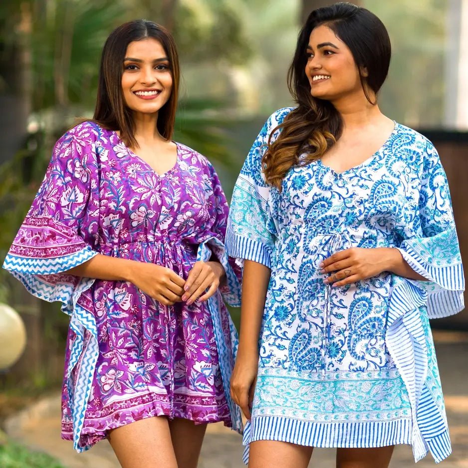 Two women modeling short kaftan-style dresses with wide sleeves. The dress on the left is purple with white floral and blue border patterns.