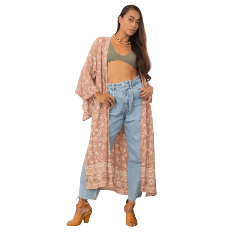 A woman modeling a long, open-front bohemian-style cardigan with a pink and beige floral pattern, worn over a sage green crop top and light blue jeans, set against a white background.