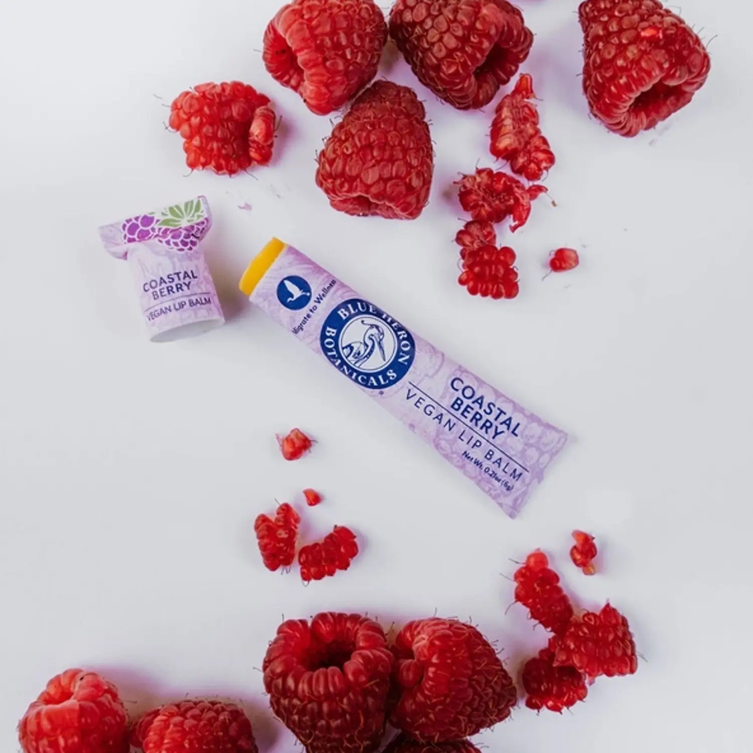 tube of vegan lip balm with SPF and red raspberry oil on table with red raspberries