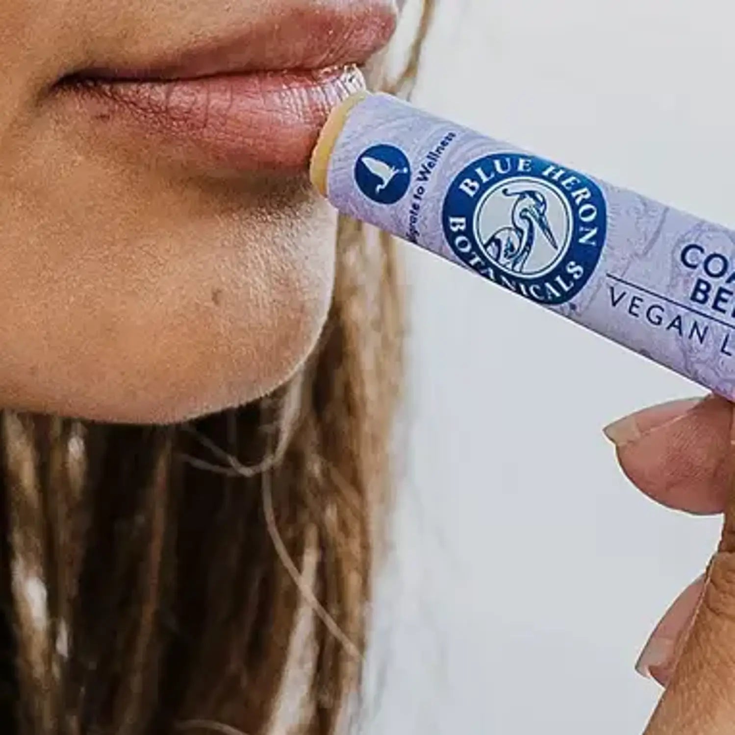 a woman applying blue heron botanicals lip balm