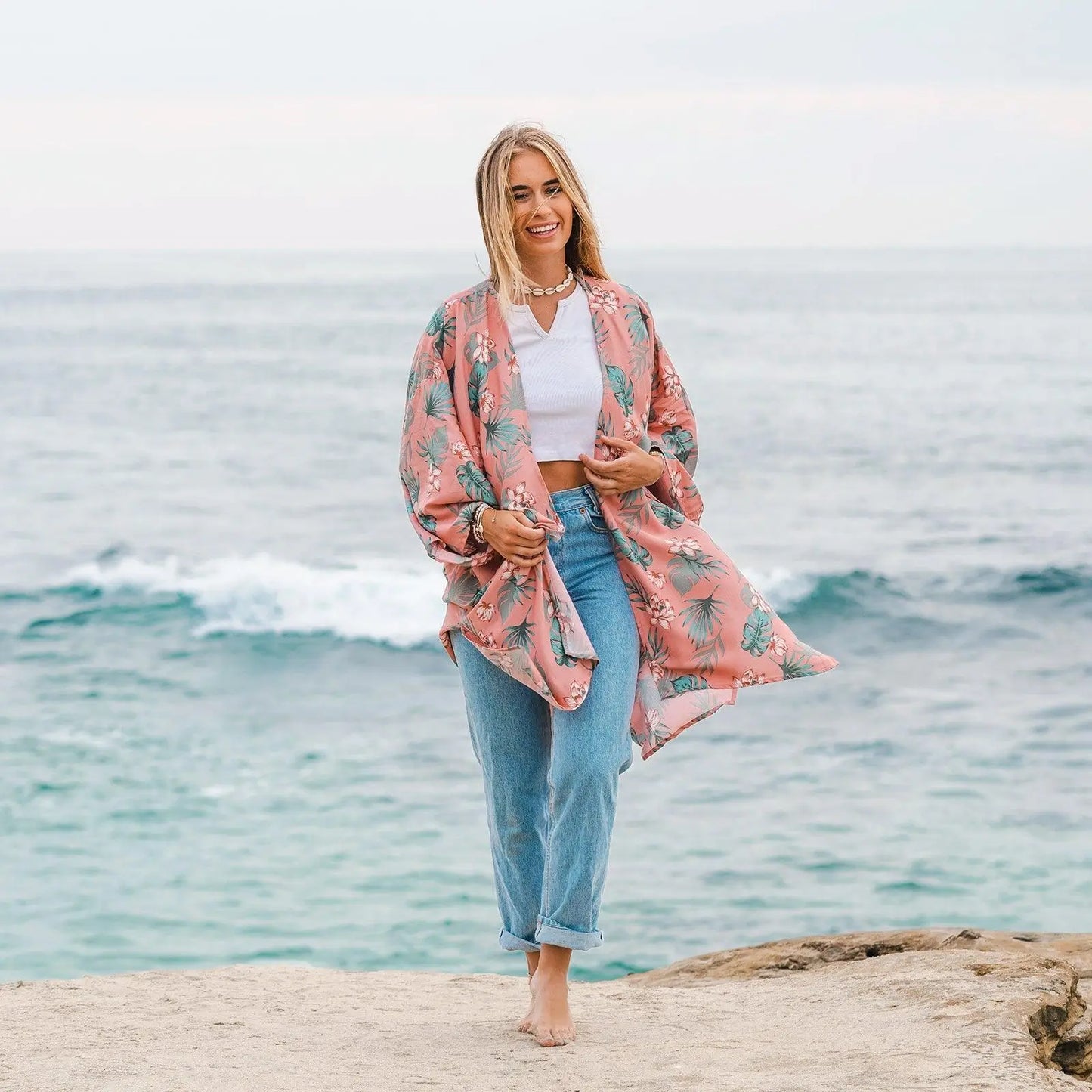 woman on beach wearing jeans and a kimono tunic top floral cover up in waimea floral print by lotus and luna