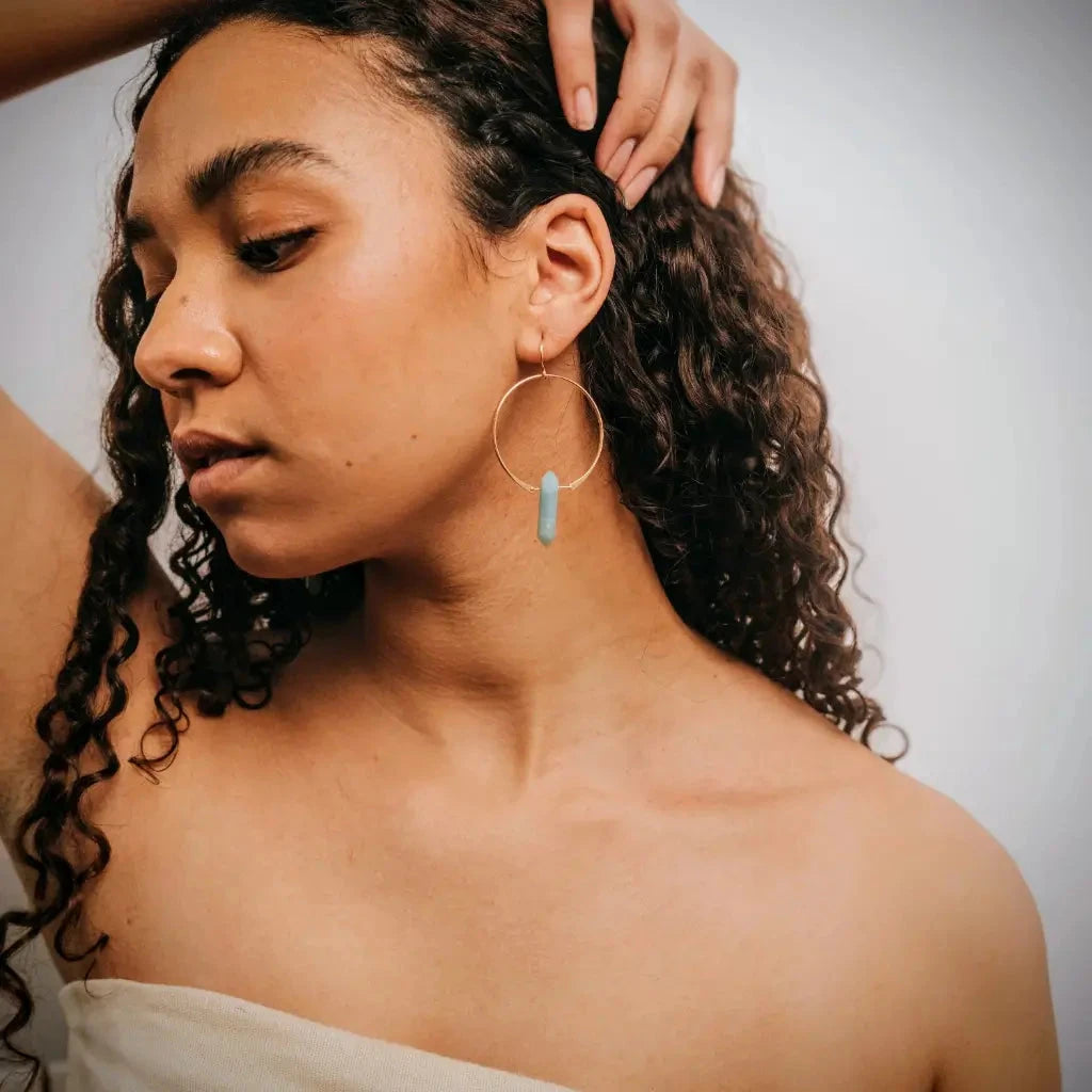 Woman wearing large gold with amazonite dangling gemstones with a neutral background