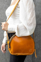 a woman carrying a brown round leather crossbody handbag